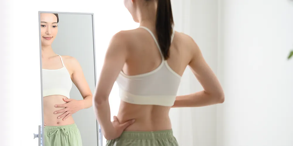 自分の身体を鏡に写して見ている女性